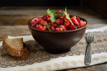 Vegetable salad, vinaigrette, in a ceramic earthenware, a folkloric bowl with a kitchen napkin on a wooden table. Village life. Home cooking.