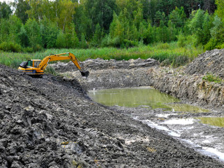 Excavator digging pond in forest. Clay soil in the foreground. Lake construction. © Yana Bo