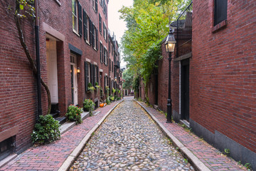 Cobled alley lined with traditional American brick row houses and gas lit lamp posts on a cloudy autumn day