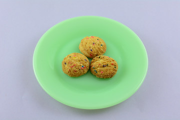 Three small bite size candy bead cookies on green plate on lavender background