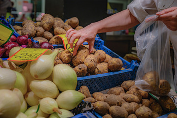 Side view of a woman picking potatoes at a farmers market. Vegetable counter.