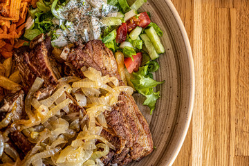 Grilled Pork ribs with fried onions and fresh vegetables on a white plate. Top View