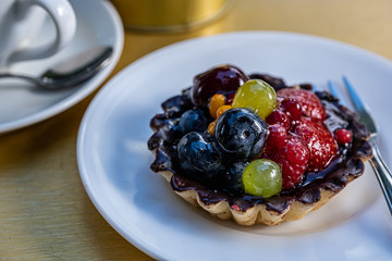 Fresh fruit tart on a white plate and a cup of coffee in a cafe. Selective focus