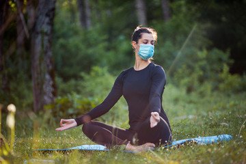 Woman practicing yoga exercise in nature with mask on face