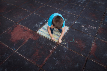 Little boy drawing with chalk and playing on the playground.