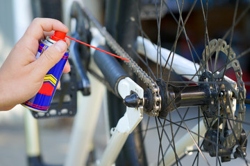 hand holding spray lubricant in his hand to lubricate the bike chain