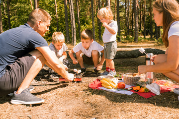 Three little boys staged a halt with a tent and a campfire in the woods in summer sunny day.campfire food