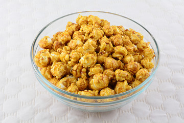 Caramel popcorn in glass snack bowl on white textured tablecloth