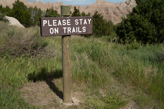 Sign reminding hikers to Please Stay on Trails, in Badlands National Park, preventing falls and other mishaps