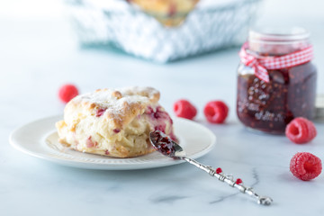 Raspberry scone with raspberry jam on a spoon and a jar of raspberry jam in behind.