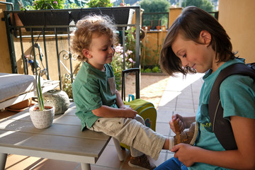 Boy helping his brother tie shoes getting ready for school, child buttoning up child's laces, young child and brother getting ready for walk with parents, siblings friendship and good relations