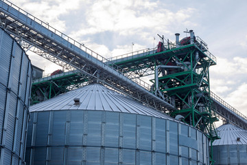 Metal grain elevator in agricultural zone. Agricultural Silos. Building Exterior. Storage and drying of grains, wheat, corn, soy, sunflower on background of cloudy sky. Agriculture.