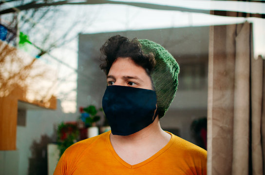 Joven con m&aacute;scara observando a trav&eacute;s de la ventana