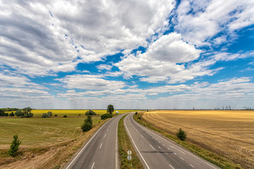 highway passing through the fields against a blue sky with beautiful white clouds