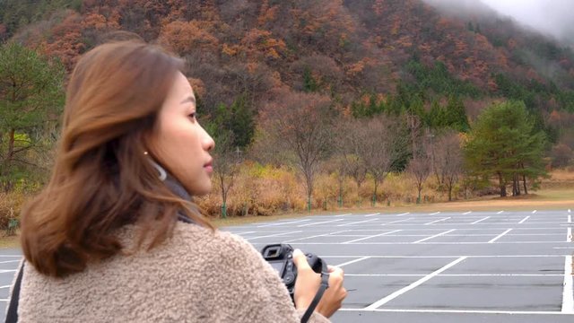 4K Happy young Asian woman tourist using digital camera taking a photo of beautiful nature red leaves forest and mountain in autumn. Beautiful lady relax and enjoy with autumn vacation travel in Japan