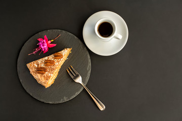 A typical Portuguese cake made of cookies called Bolo de Bolasa with cream, pecans, black and white chocolate on a black slate with a fork, espresso and a flower on a black background.Top view Flatlay