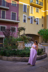 Fototapeta na wymiar beautiful young pregnant girl in a purple dress stands in the old city