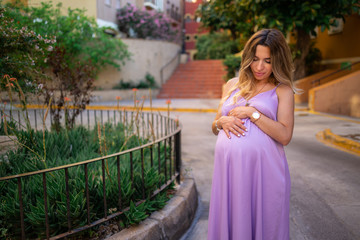 beautiful pregnant girl holding her belly and sitting on a bench overlooking the garden