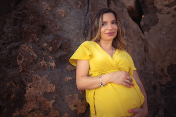 young pregnant girl on brown rocks view in yellow dress 