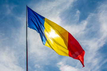 Beautiful low angle shot of the Romanian flag waving on a sunny bright sky background