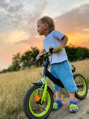 Little light-skinned child on a bright bike ride, rides across the field at sunset in summer. Free space.Active lifestyle concept.