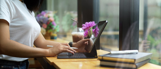 Obraz na płótnie Canvas Female hands using digital tablet on wooden table beside window in cafe