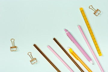 Flat lay with stationery for school or office. Pink and golden colored pencils, pens and metal paperclips. School equipment. Top view with copy space.