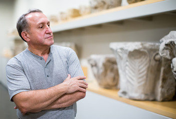 concentrated middle aged man examining exposition in museum hall of ancient sculpture