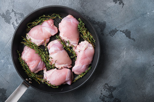 Uncooked chicken thighs  with thime on iron cast pan on grey background, flat lay with copy space
