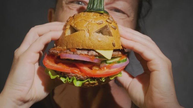 Woman eating beef burger in shape of pumpkin for halloween close-up.