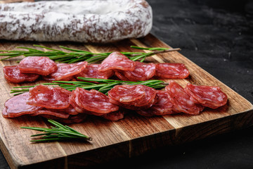 Fuet salami wurst cut in slices and whole sausage on black textured surface