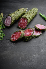 Fuet salami sausage in herbs on black textured surface