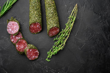 Fuet salami sausage in herbs on black background, flat lay with copy space
