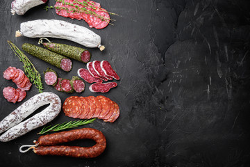 Set of dry cured salami, spanish sausages, slices and cuts on black textured surface, topview with...