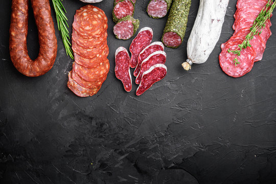 Set of dry cured salami, spanish sausages, slices and cuts on black background, top view with copy space