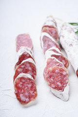 Variety of dry cured fuet and chorizosalami sausages, whole and sliced on white textured background