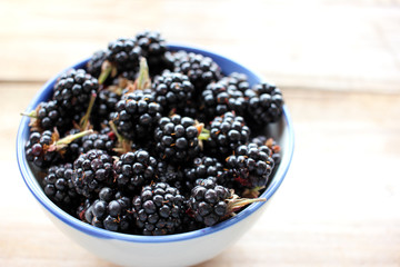 Bowl of fresh blackberries on wooden background. Top view. Summer berries on the table
