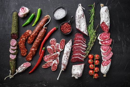 Set of various spanish dry cured salami sausages slices and whole cuts on balck background, flat lay