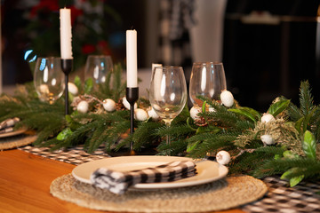 The festive Christmas table is decorated with branches of a Christmas tree, candles and garlands. Cozy home Christmas atmosphere.