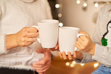 Cozy friendly family christmas home environment. Mom and daughter drink hot tea. Close up of white cups of tea in hands.