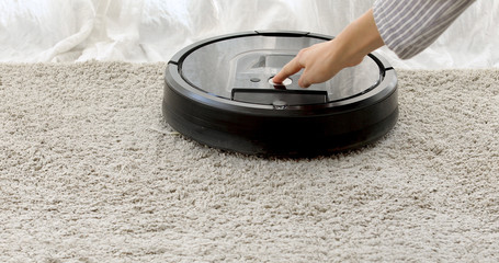 woman sets the program to the robot vacuum cleaner and it starts moving, cleaning the floor by the...