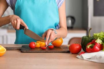 Beautiful young woman making vegetable salad in kitchen