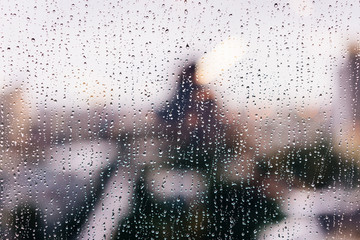 Raindrops on windows glass in the golden hour with blur highrise buildings in the background.