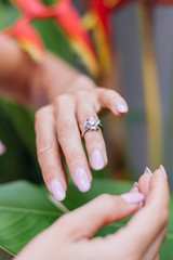 Close shot of womans hands wearing ring on finger on background of tropical leaf and red flowers. 