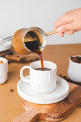Woman pouring hot coffee from pot into cup on table