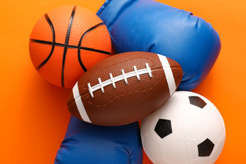Sports balls with boxing gloves on color background