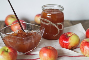 Season for making jam for future use. Apple jam in a salad bowl on a napkin on a wooden table with jars of jam in the background.