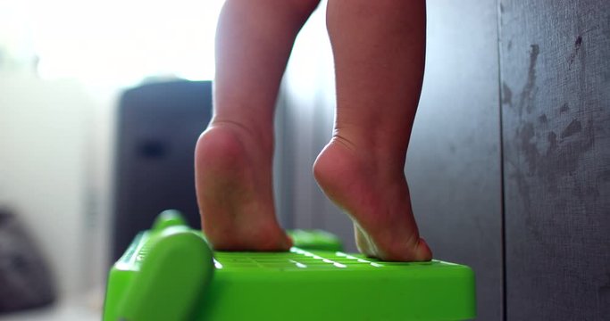 Cute baby tiptoeing by kitchen sink. Toddler child tiptoe reaching for object
