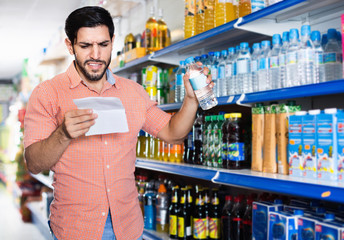 Happy cheerful man is choosing water with help note list in supermarket.