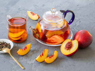 Fresh peach tea in a mug and glass teapot on a grey background with copy space.